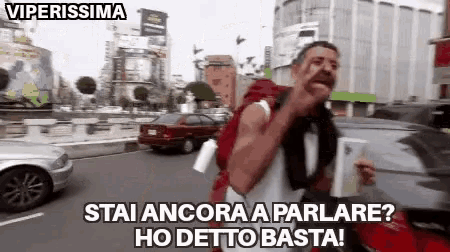 a man with a backpack is walking down a street and says viperissima stai ancora a parlare ho detto basta .