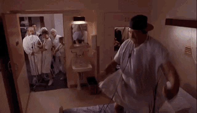 a man in a hospital gown is sitting on a hospital bed while a group of doctors and nurses look on .