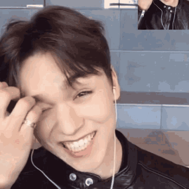 a young man wearing headphones and a leather jacket is smiling while talking on a video call .