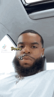 a man with a beard is sitting in a car with the name drew written on his face