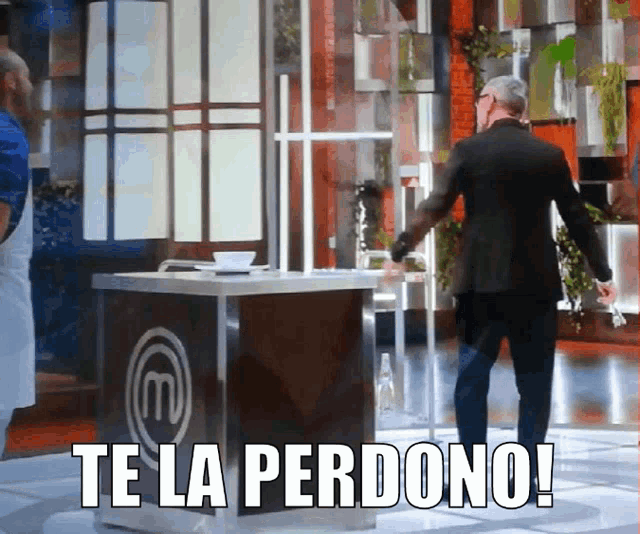 a man in a suit stands in front of a table with the letter m on it and says te la perdono