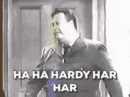 a man in a suit and tie is standing in front of a door and says " ha ha hardy har har " .