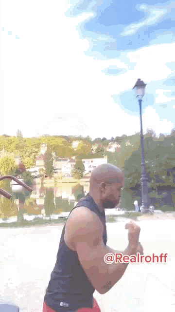 a man is flexing his muscles in front of a lake and a street light with the hashtag @realrohff