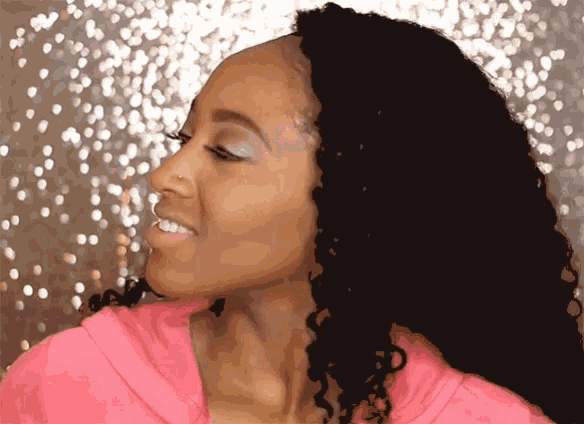 a woman with curly hair is wearing a pink sweatshirt