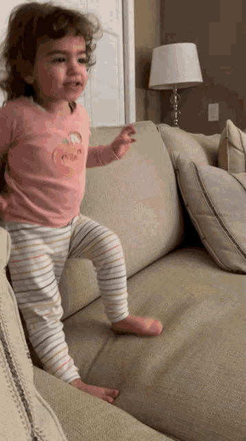 a little girl standing on a couch wearing a pink shirt with an apple on it