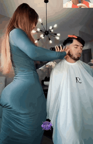 a woman in a blue dress is cutting a man 's hair with a r logo on his shirt
