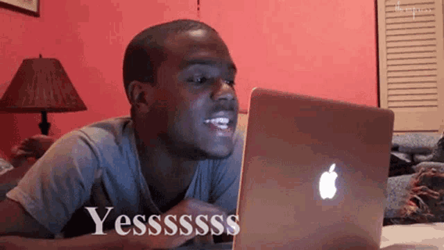 a man laying in front of an apple laptop that says yesssss on it