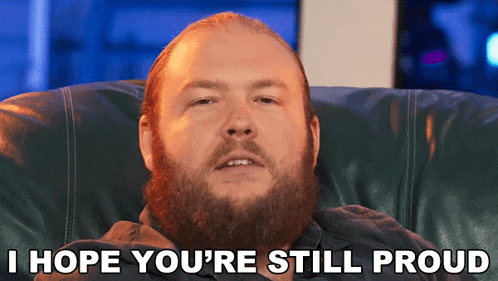 a man with a beard is sitting in a chair with the words i hope you 're still proud below him