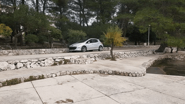 a silver car is parked on the side of a road near a stone wall
