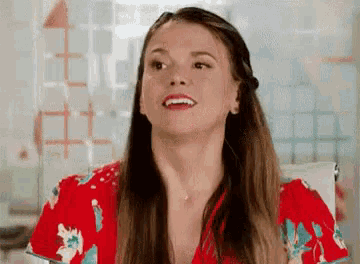 a woman in a red floral shirt is sitting in a chair and smiling .