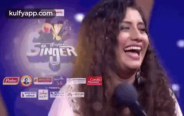 a woman is laughing while singing into a microphone in front of a screen that says super singer .