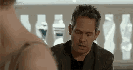 a man in a suit is sitting at a table with a woman in a bra .