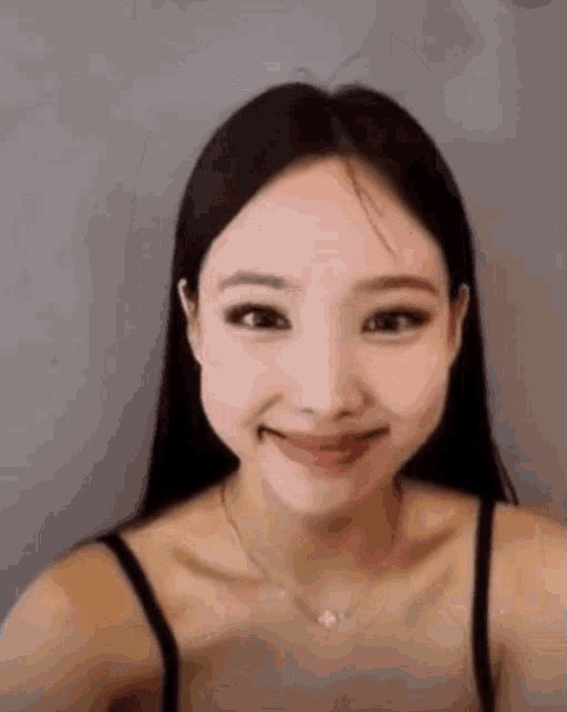 a close up of a woman wearing a black tank top and a necklace smiling .