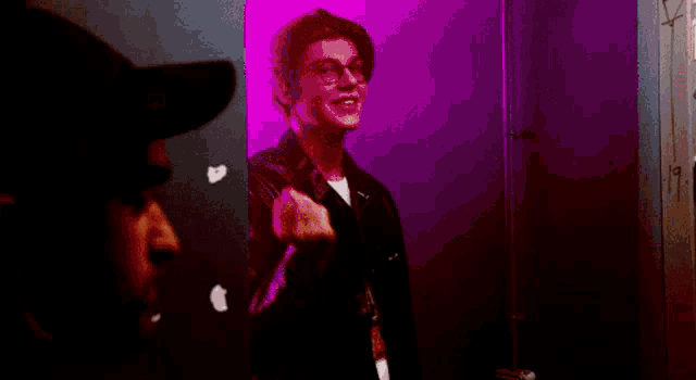 a man wearing glasses and a hat is standing in front of a pink wall .