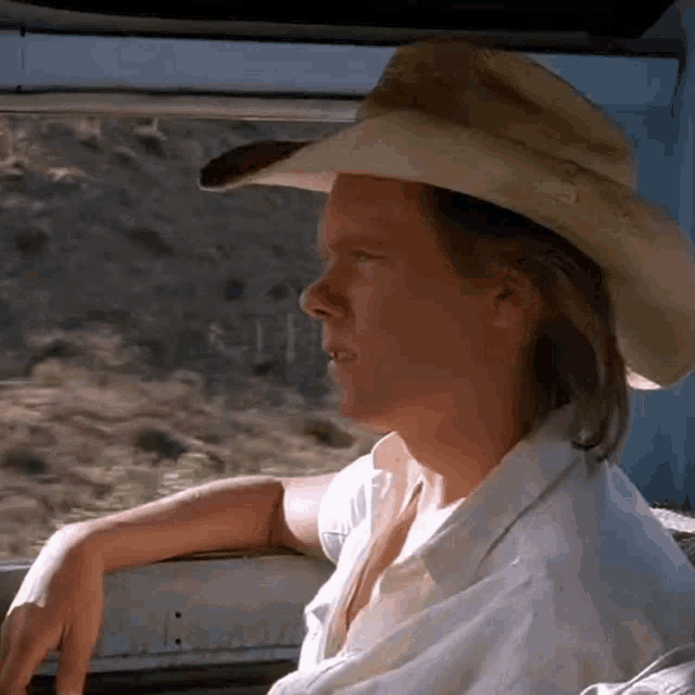 a man wearing a cowboy hat and a white shirt is looking out a window