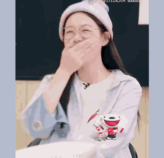 a girl wearing glasses and a hat covering her mouth with her hands