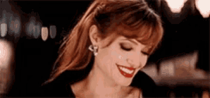 a woman with red hair and red lips is smiling and wearing earrings .