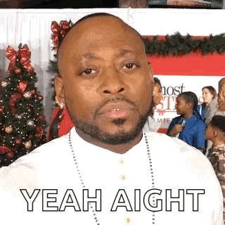 a man with a beard and a white shirt is standing in front of a christmas tree .