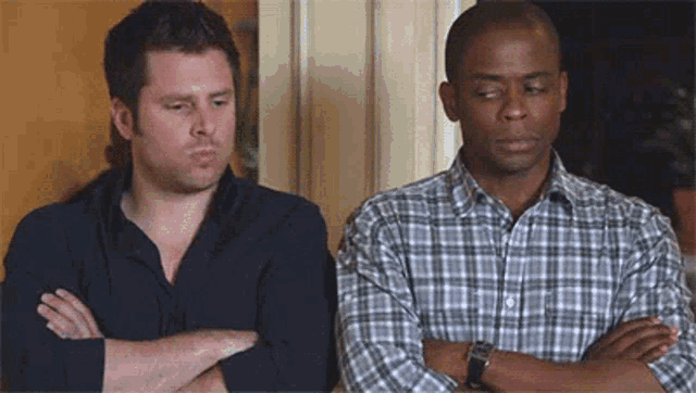 two men are standing next to each other with their arms crossed . one of the men is wearing a plaid shirt .