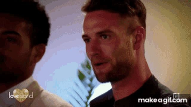 a man with a beard is standing next to another man on a love island show .