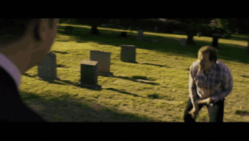 a man in a suit stands in a cemetery looking at another man