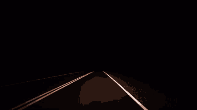 a man in a white shirt is walking down a dark road