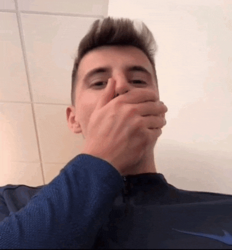 a man covering his mouth with his hand while wearing a nike shirt