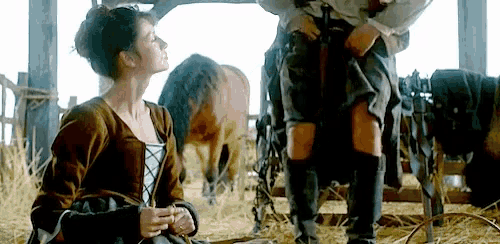 a man and a woman are standing next to each other in a barn with horses .