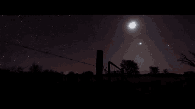 a barbed wire fence is silhouetted against a starry sky