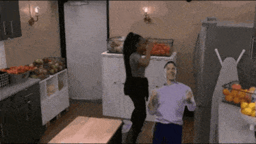 a man and a woman are dancing in a kitchen with vegetables in the background