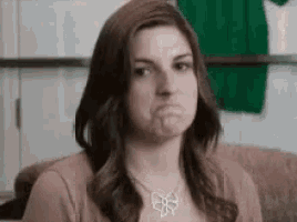 a woman wearing a necklace and a brown shirt is making a funny face .