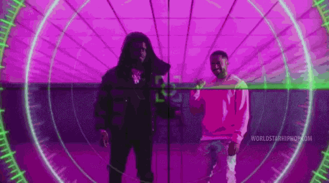two men are standing next to each other in a purple room with a green light behind them .