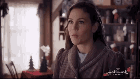 a woman is standing in a room with a christmas tree in the background and looking at something .