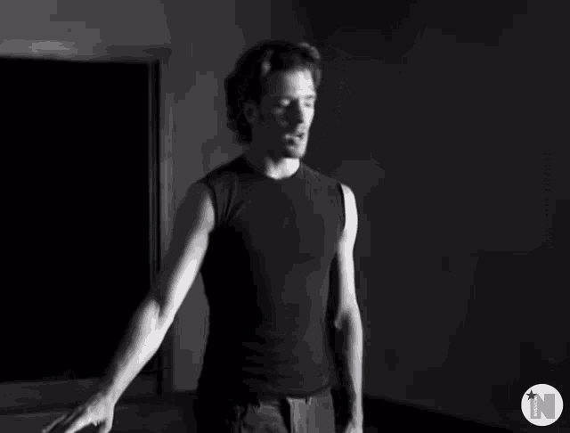 a man in a black tank top stands in a dark room