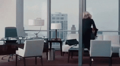 a woman in a black dress is walking through a glass door in an office