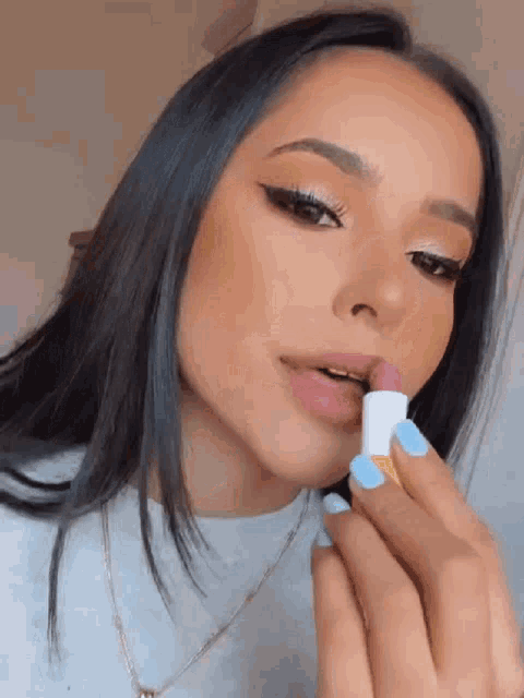 a woman with blue nails is applying lipstick on her lips