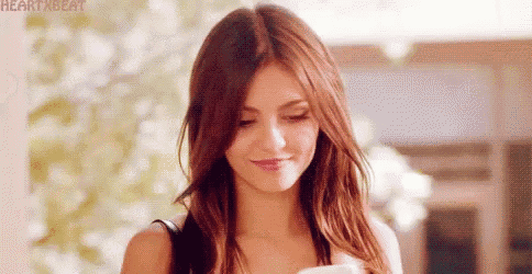 a woman with long brown hair is smiling and looking down at something .