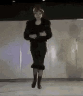 a woman in a black dress and boots is jumping in the air on a stage .