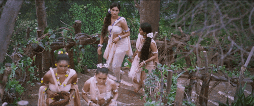 a group of women standing in a forest wearing white dresses