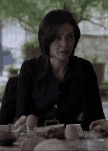 a woman in a black shirt sits at a table with eggs