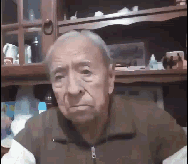 an elderly man in a brown jacket is sitting in front of a glass cabinet .