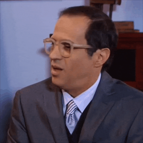 a man wearing glasses and a suit is making a surprised face