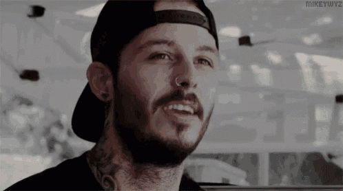 a man with a beard and a nose ring is wearing a baseball cap .