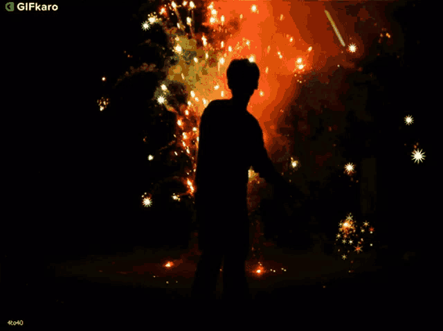 a man stands in front of a fireworks display with a gifkaro logo in the lower right corner