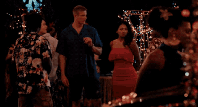 a man in a blue shirt is talking to a woman in a red dress at a party