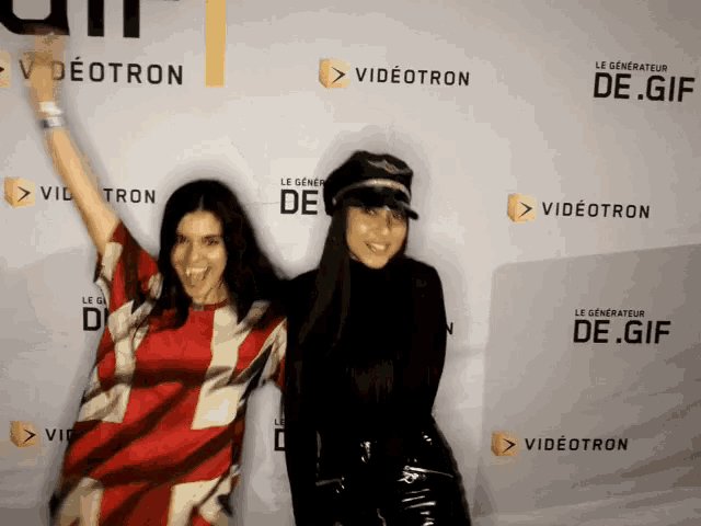 two women pose for a photo in front of a wall that says videotron