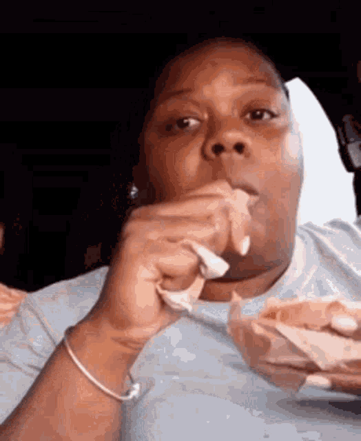 a woman is eating a hamburger in a car while holding a napkin .