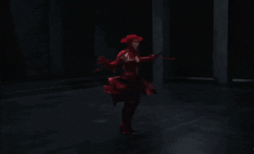 a woman in a red dress is dancing in the dark