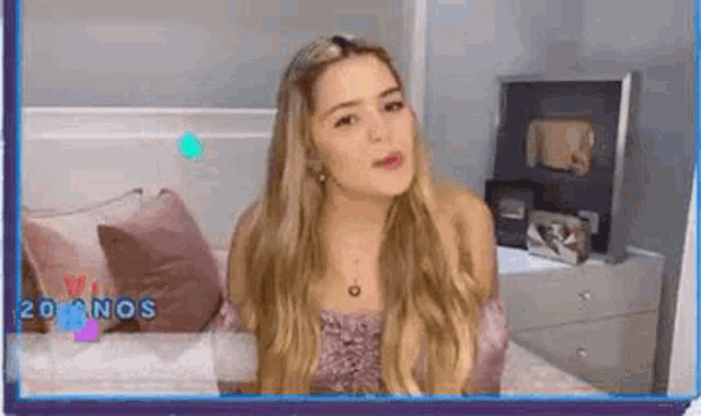 a woman with long blonde hair is sitting on a bed in a bedroom .