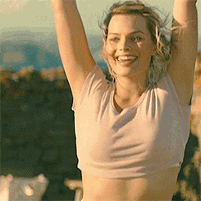 a woman in a pink crop top is smiling and raising her arms in the air